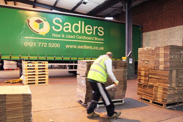 A warehouse worker wraps a pallet of used boxes to send for reuse